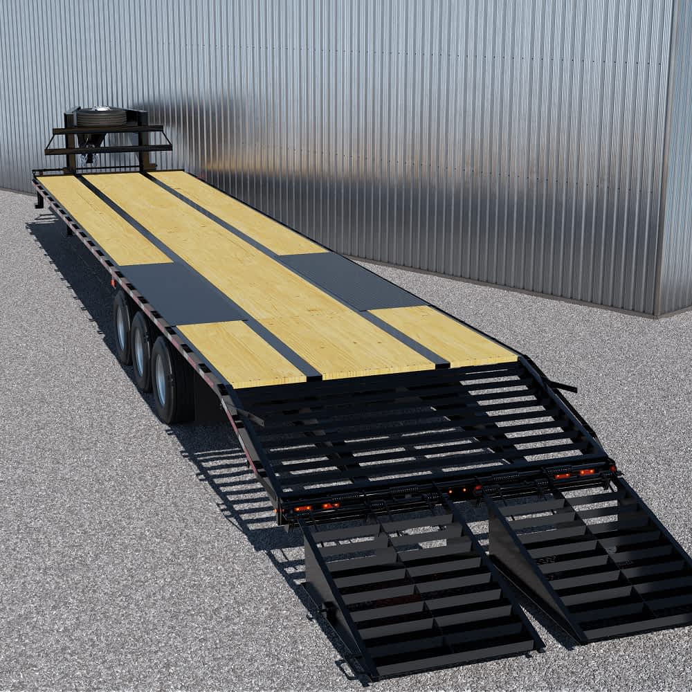 A long, black Texas Pride flatbed trailer with a pierced frame wooden deck and two fold-down ramps at the rear is parked on a gravel lot in front of a corrugated metal building. The trailer has multiple axles and a gooseneck hitch.
