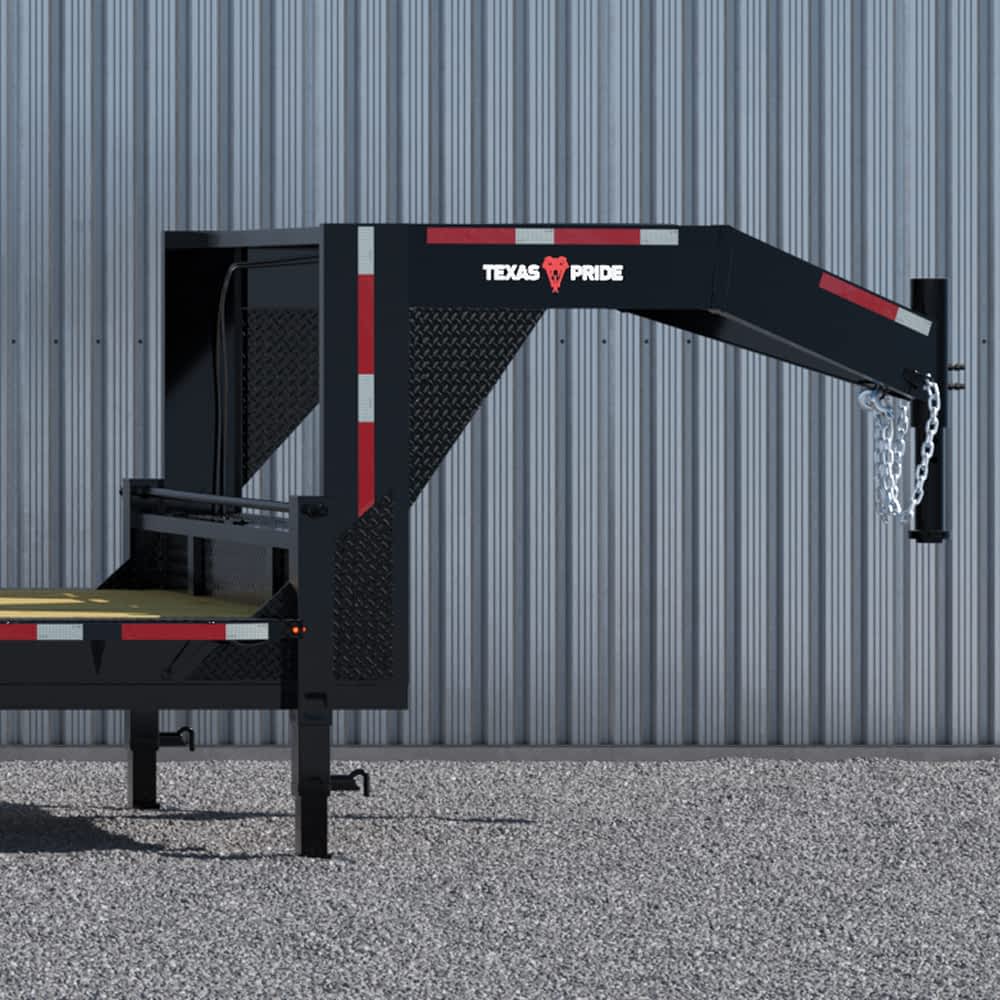 A portion of a black Texas Pride gooseneck lowboy trailer is shown against a light gray metal wall. The trailer features the white "TEXAS" and "PRIDE" lettering flanking a red longhorn skull logo, along with red and white reflective safety markings and a heavy-duty chain.