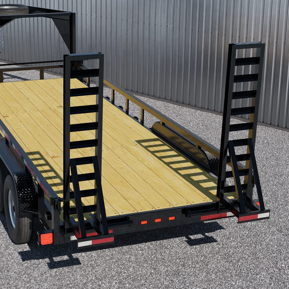 The rear of a black Texas Pride lowboy trailer with a wooden deck and two black, ladder-style ramps is shown parked on a gravel surface. Red and white reflective tape is visible on the trailer's edges, and a light gray metal wall forms the backdrop.