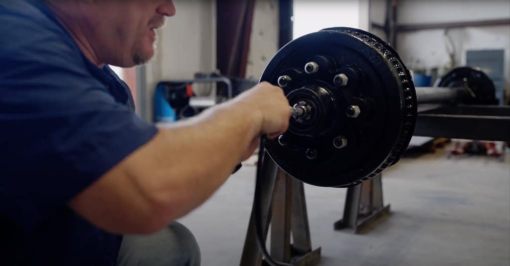 Man shows how to add more grease from a grease gun to a trailer axle.