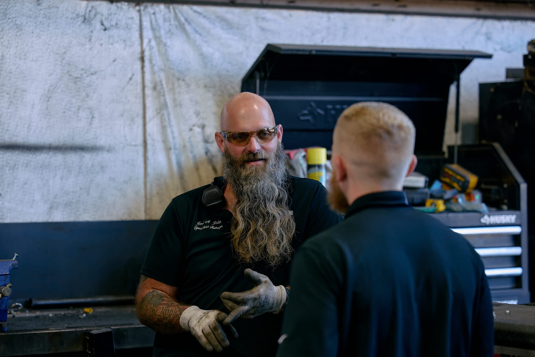 Two men talk in a Texas Pride Trailers workshop. One man with a long beard gestures while talking to another man.