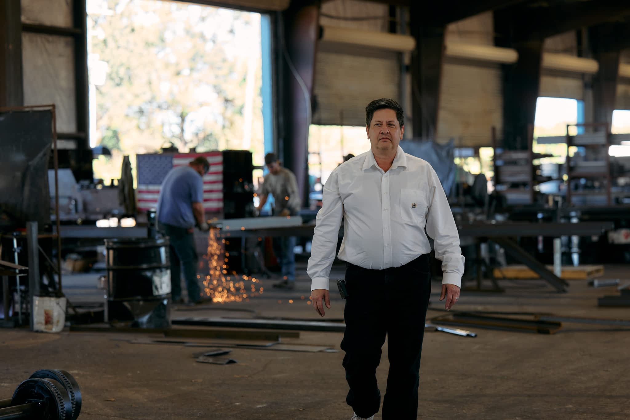 James Bray walks through a Texas Pride Trailers manufacturing facility, with workers welding in the background and an American flag hanging.