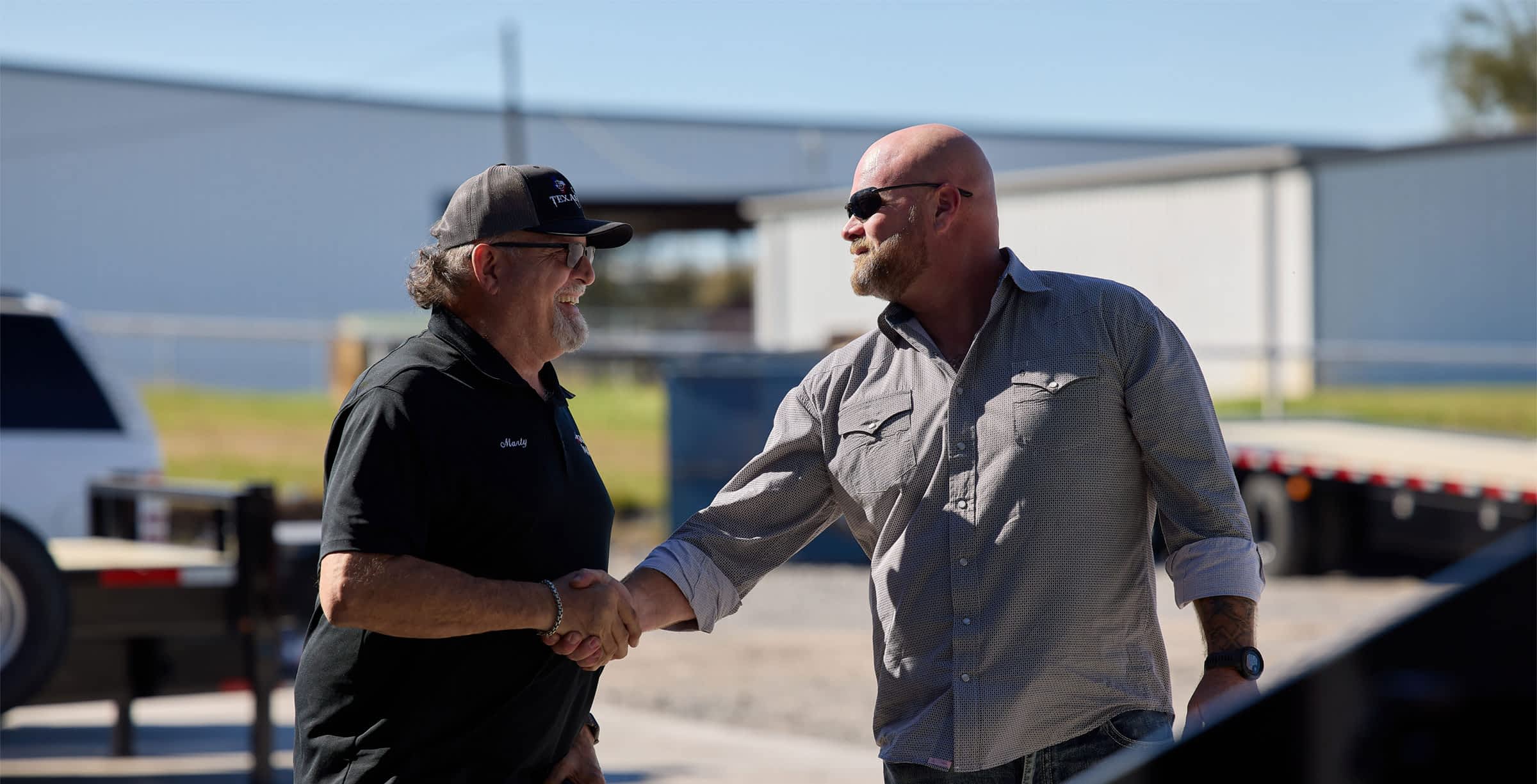 Texas Pride Trailers team member shaking hands with a customer outside the manufacturing facility, highlighting personalized service and customer satisfaction.