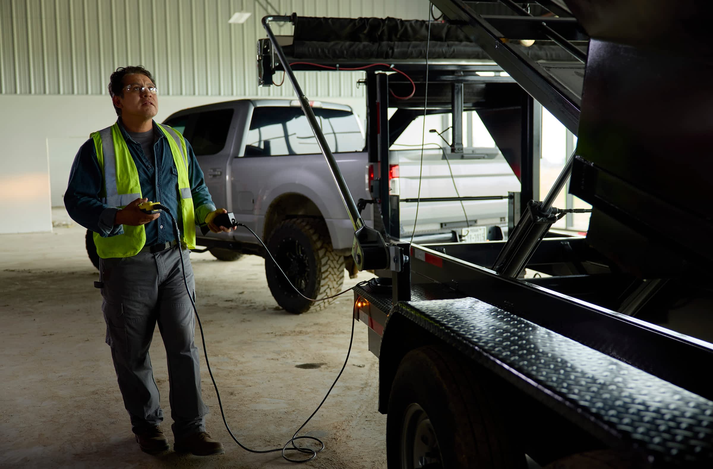 Worker operating a Texas Pride trailer lift using hydraulic controls inside a garage.