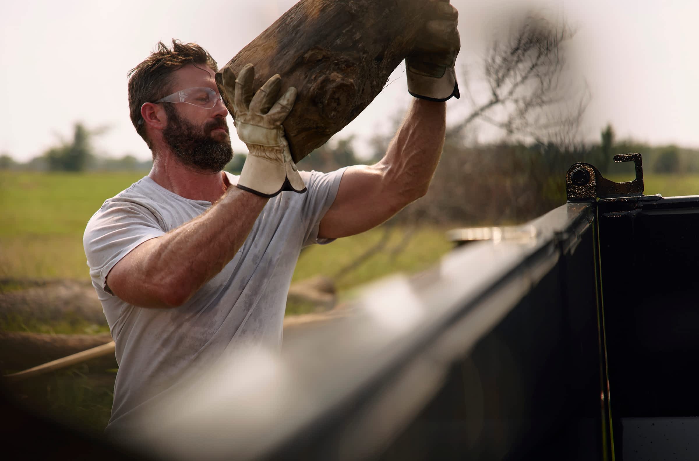 Close-up of a worker loading heavy logs by hand into a Texas Pride trailer.