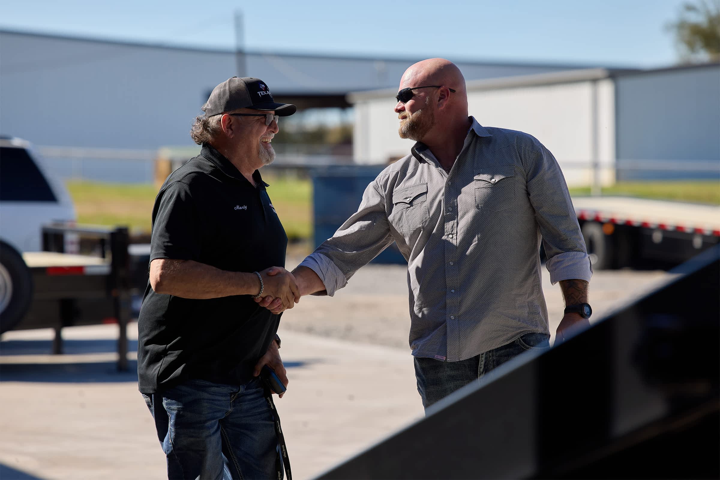 Two men shaking hands outside a Texas Pride trailer facility, symbolising customer service and satisfaction.
