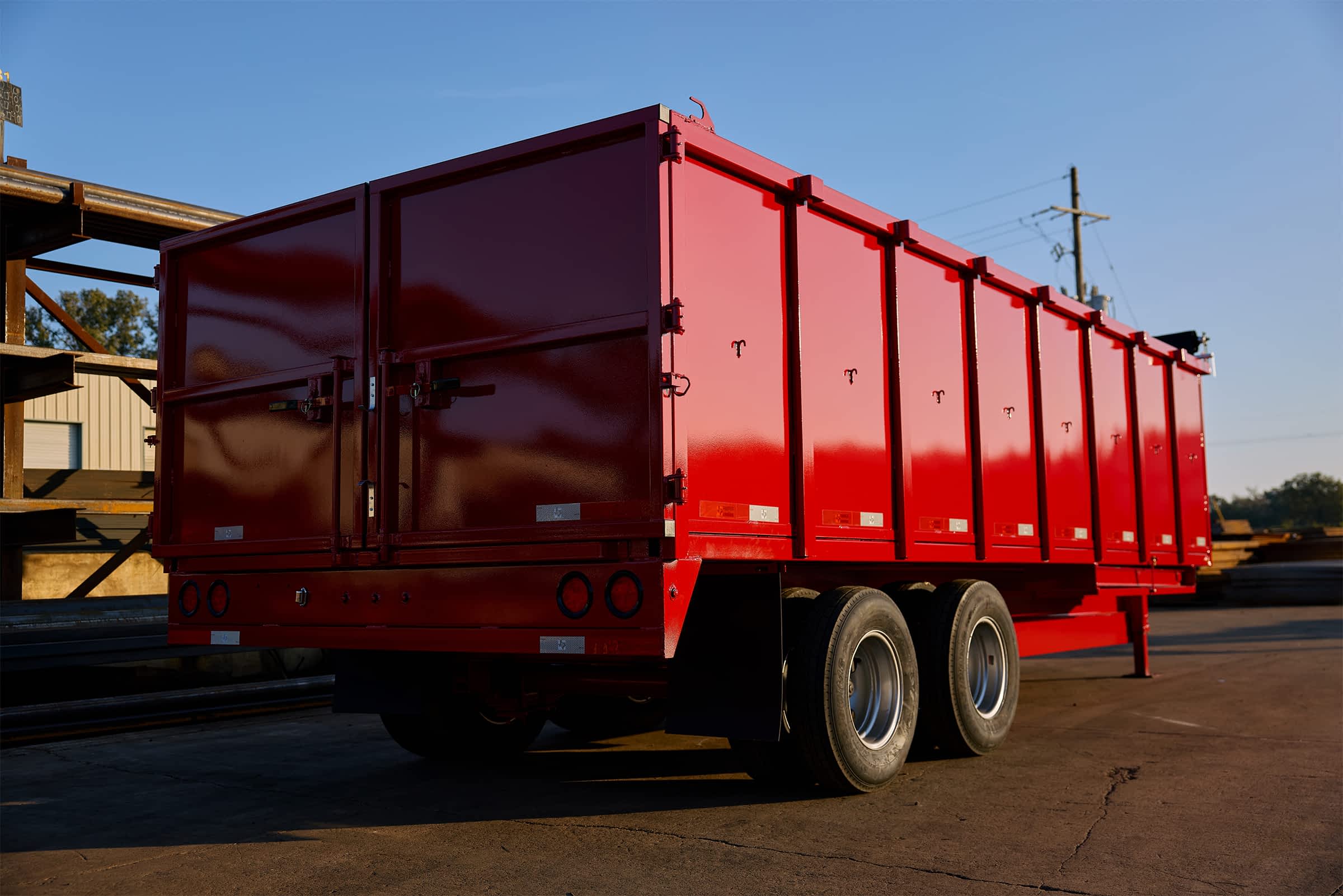 Bright red Texas Pride dump trailer parked in the yard, viewed from the rear and side angle.