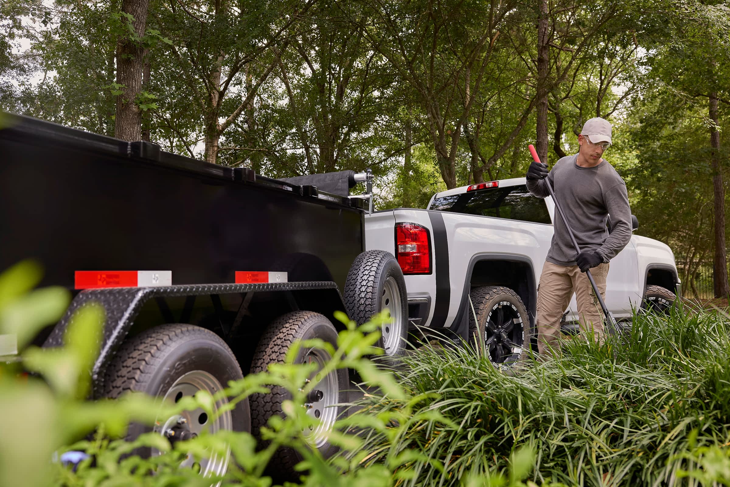 Worker standing next to a Texas Pride trailer hitched to a truck, ideal for landscaping and transport tasks.