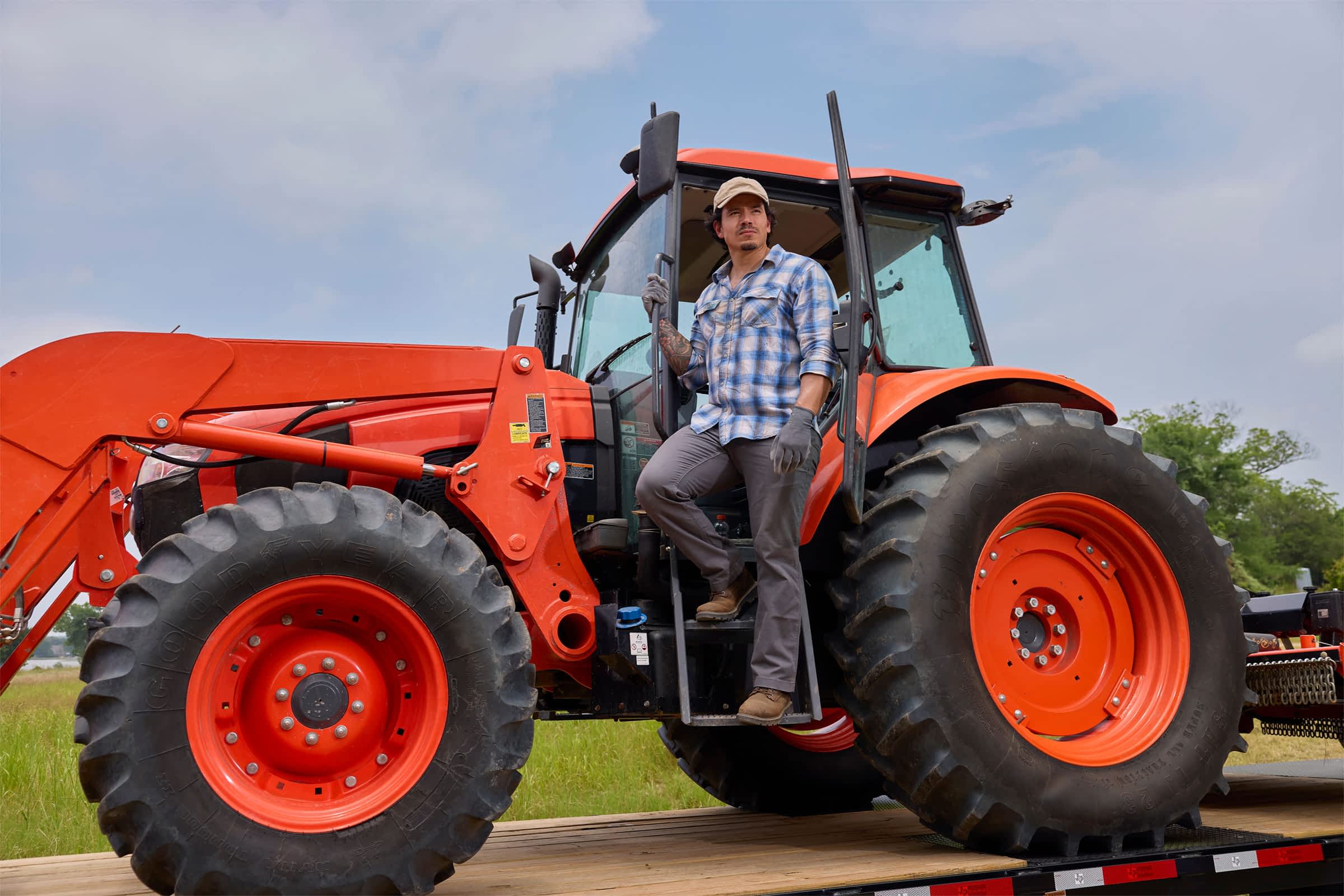 A man in a plaid shirt and hat climbs out of a large farming vehicle.