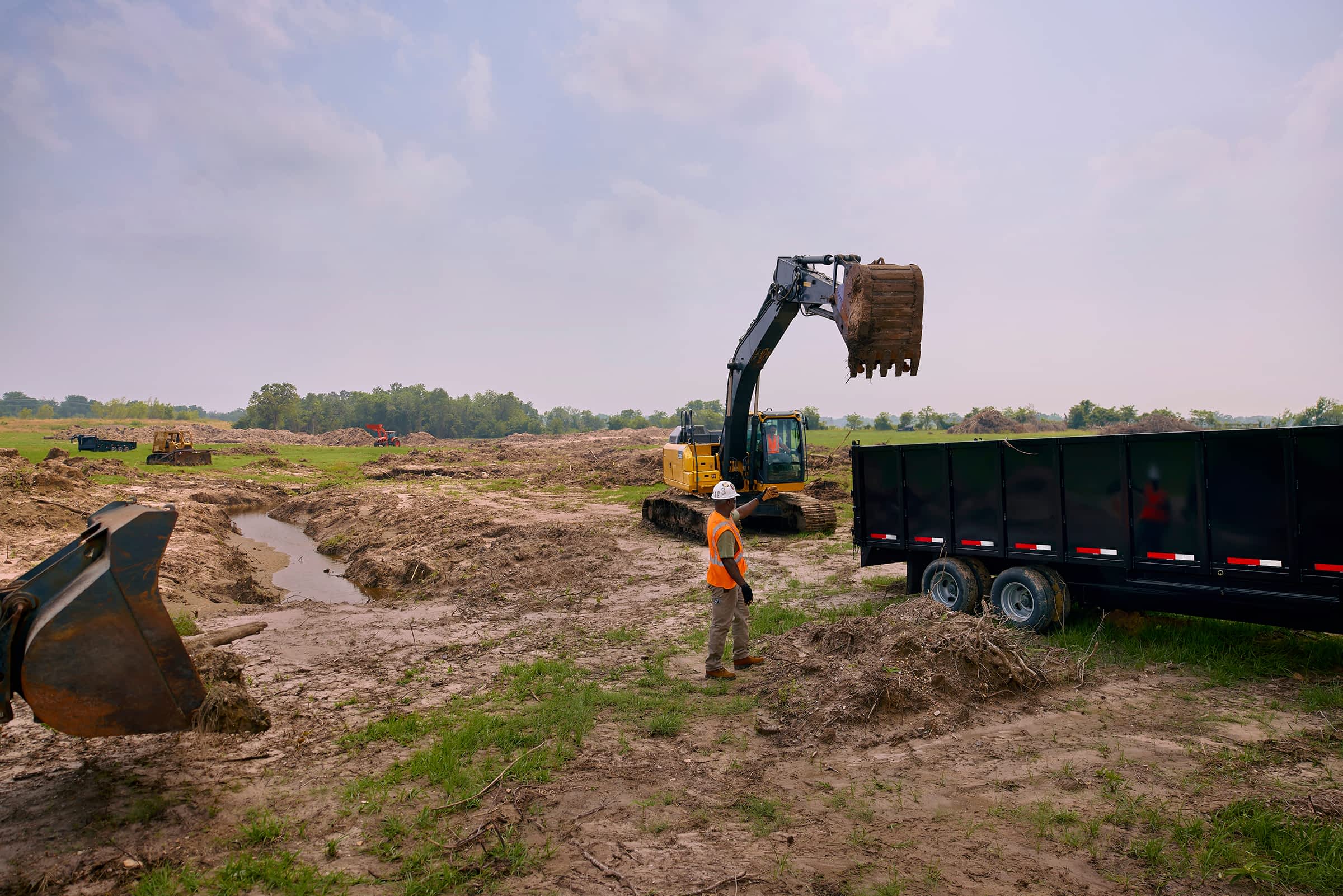 Excavator loading soil into a Texas Pride dump trailer on a construction site.