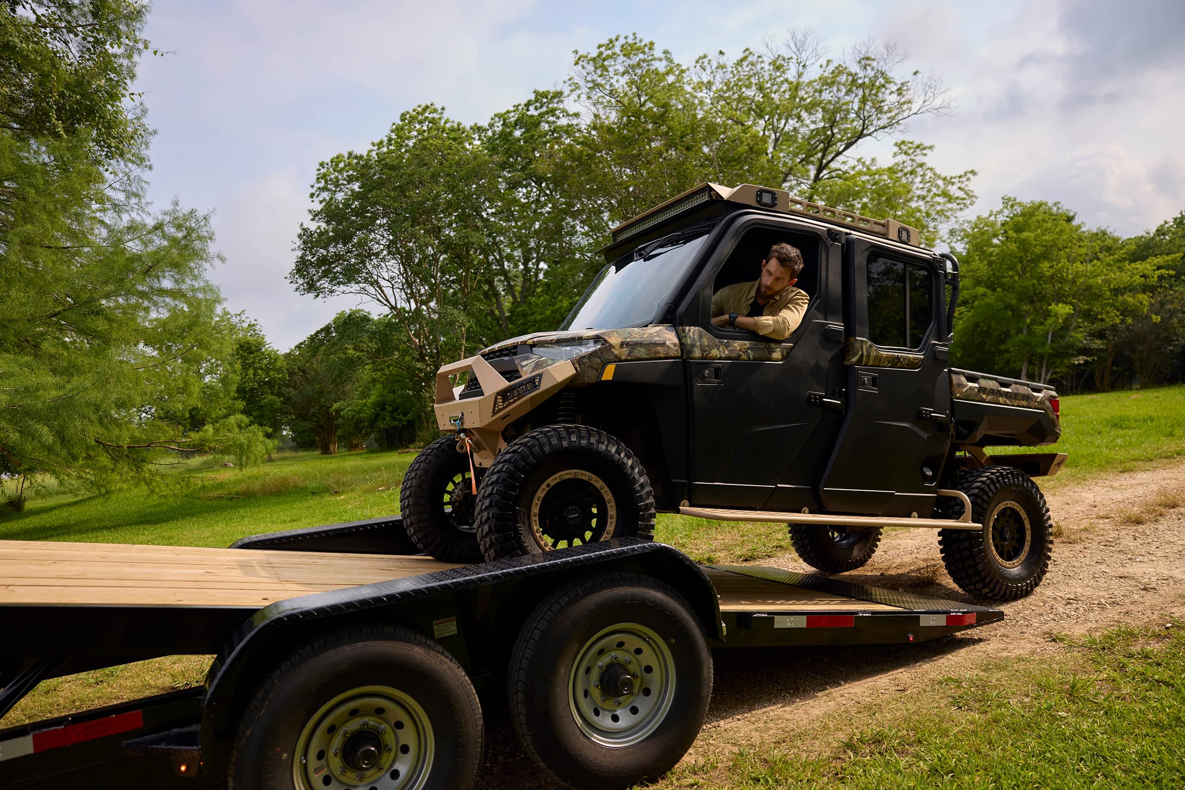 Man loading an off-road vehicle onto a Texas Pride equipment trailer in a rural setting.