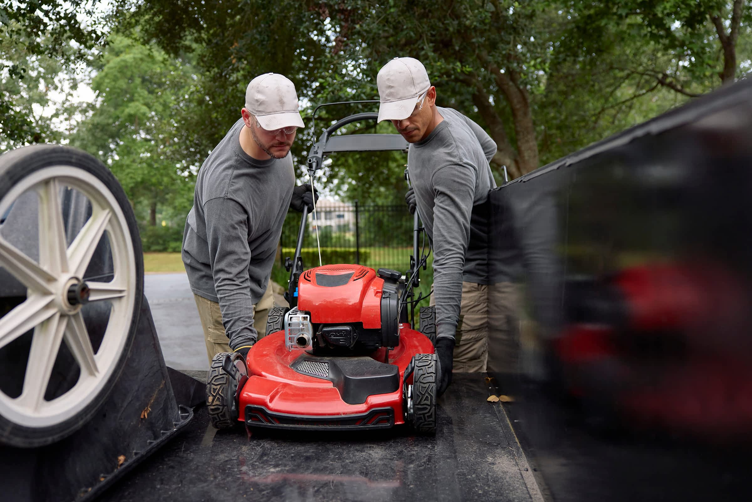 Two workers loading a lawnmower onto a Texas Pride trailer, demonstrating ease of use and accessibility.