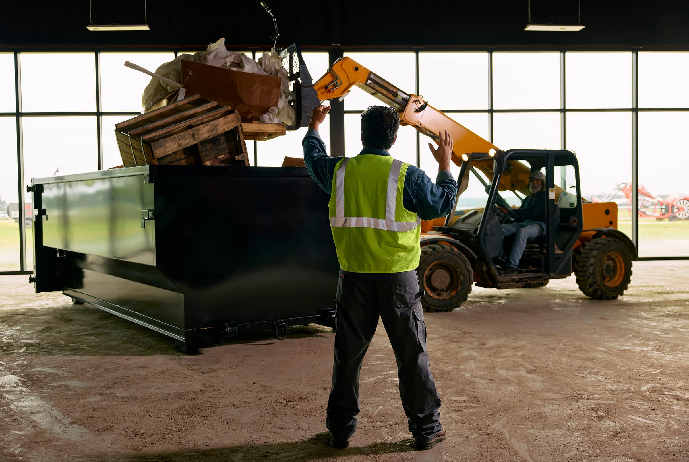 Worker directing forklift loading heavy industrial materials into a Texas Pride trailer inside a warehouse.