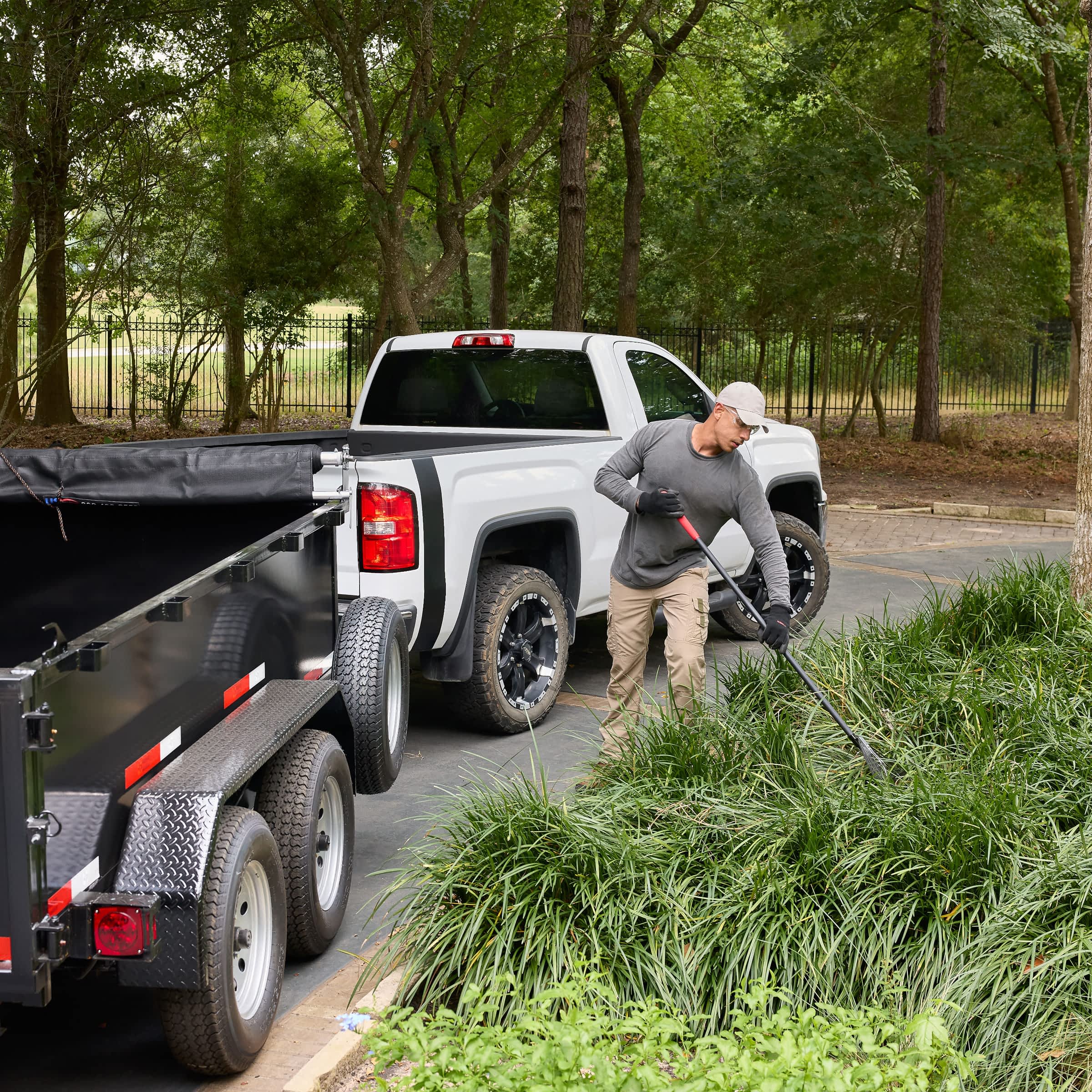 A man works on landscaping in front of a nice white truck with a dump trailer.