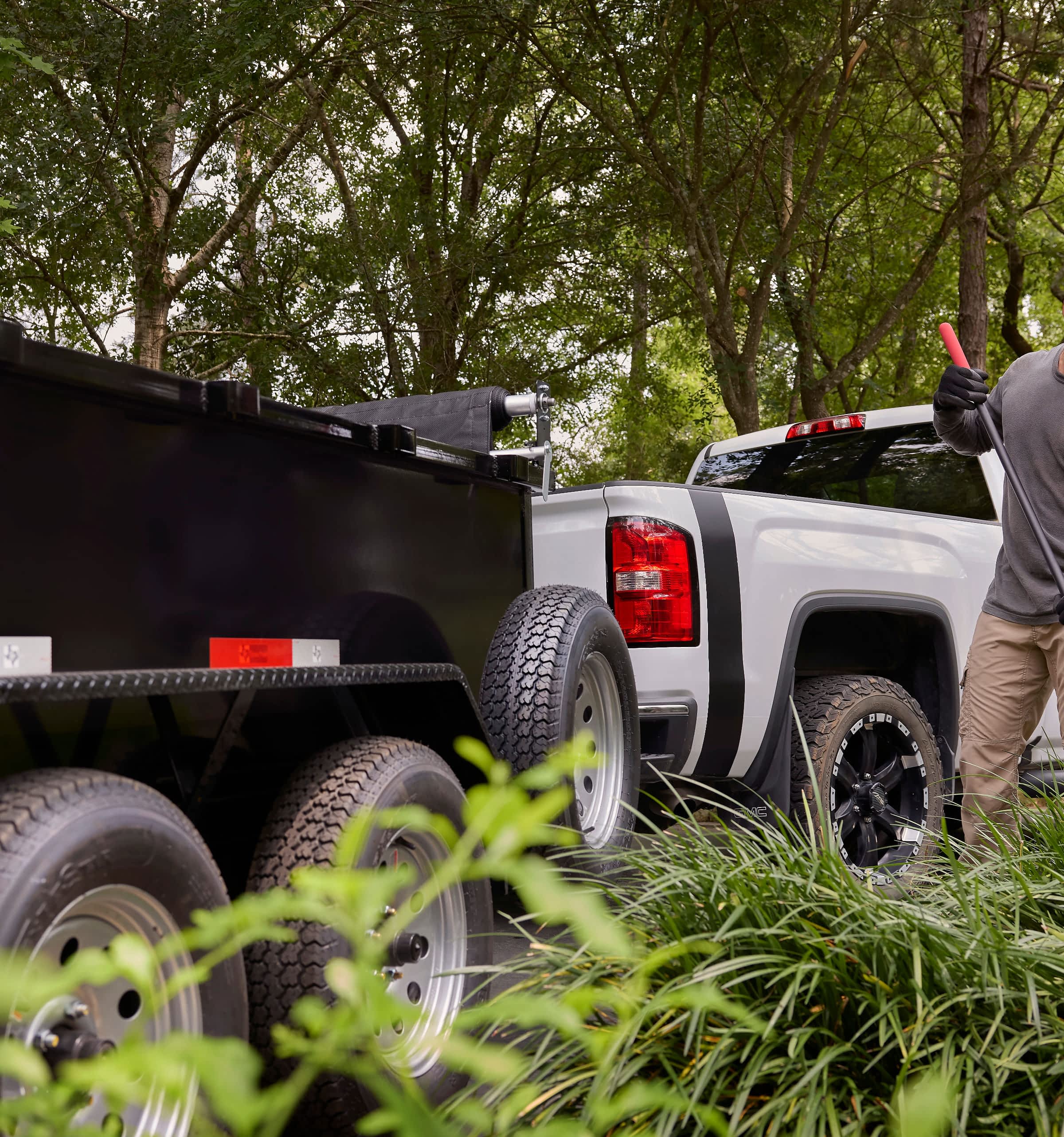 A man works on landscaping in front of a nice white truck with a dump trailer.