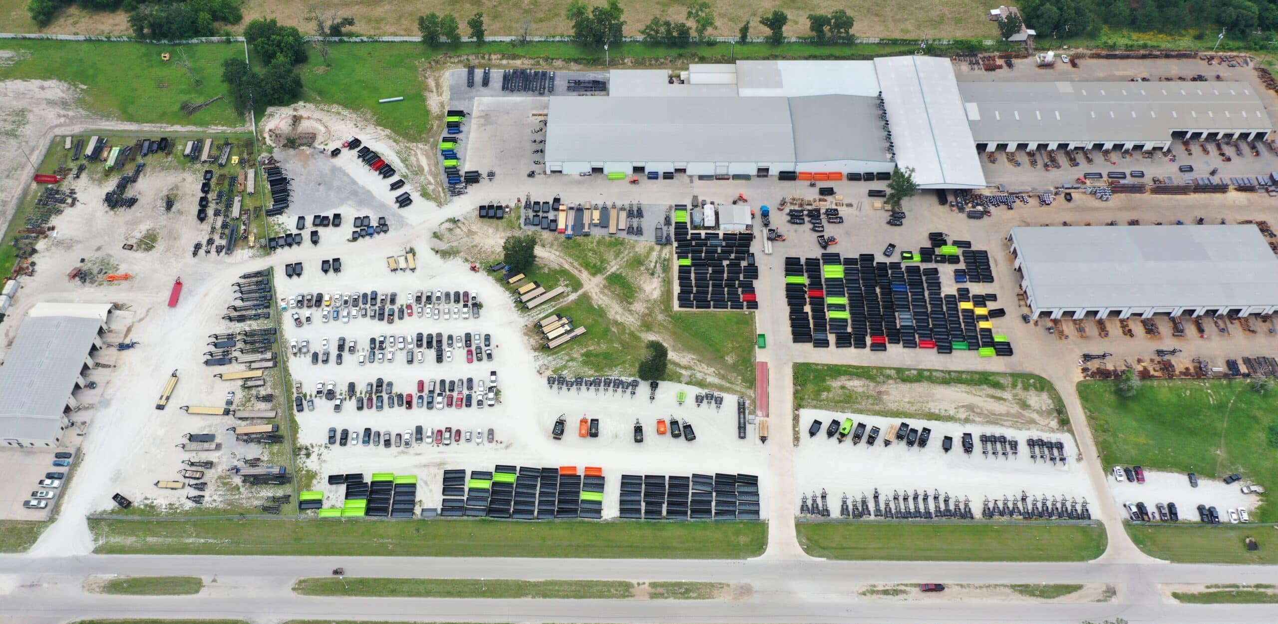 Aerial view of the Texas Pride Trailers manufacturing facility in Madisonville, Texas, showing multiple warehouses, rows of trailers in various colors, employee vehicles, and equipment yards—capturing the scale of operations behind the company’s 100,000-trailer milestone.