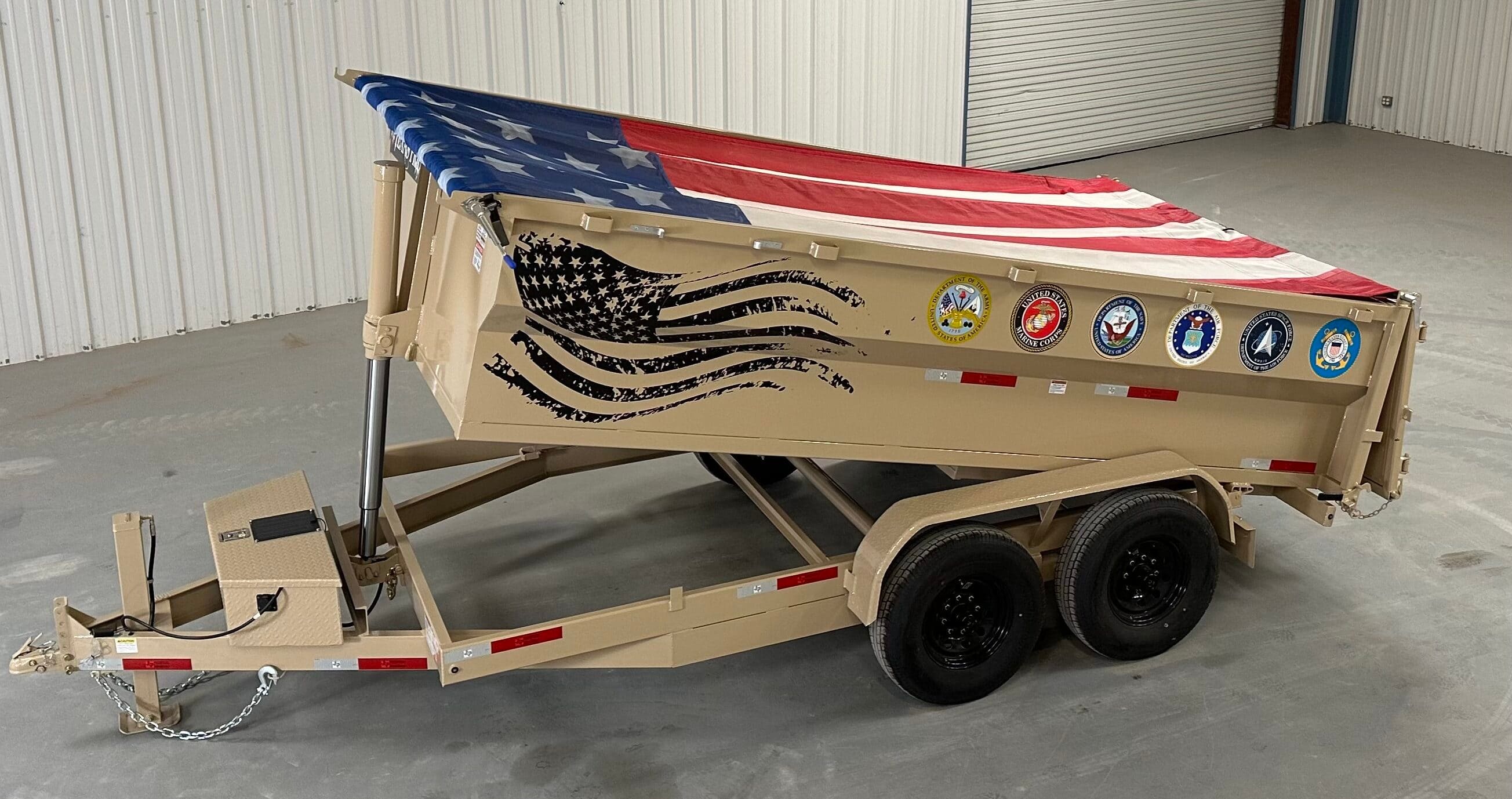 Texas Pride’s 100,000th trailer—a tan gooseneck dump trailer featuring an American flag tarp, military branch decals, and a black stylized flag graphic on the side.