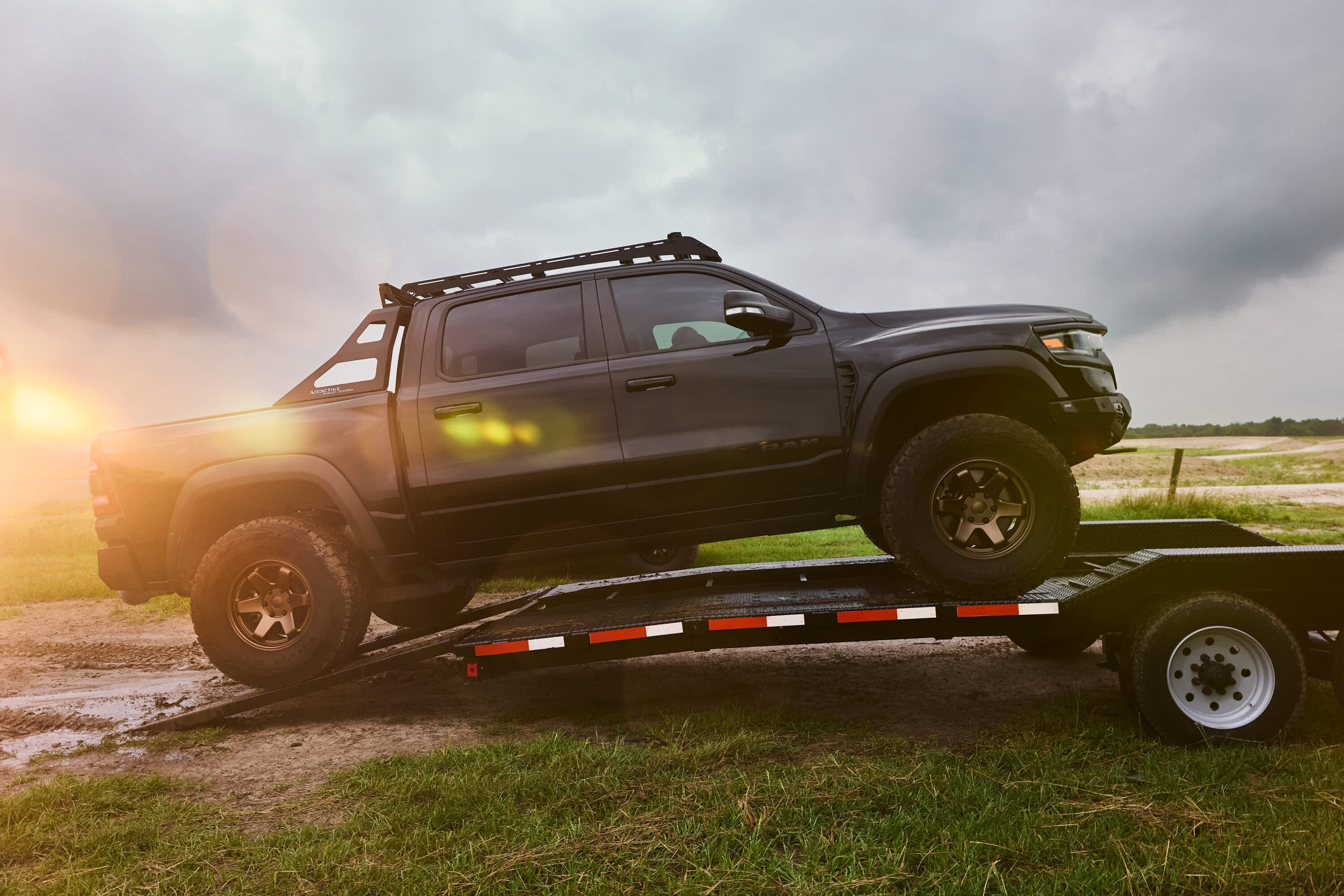 A black Ram truck is driven up ramps onto a Texas Pride Trailers car hauler trailer in a field.