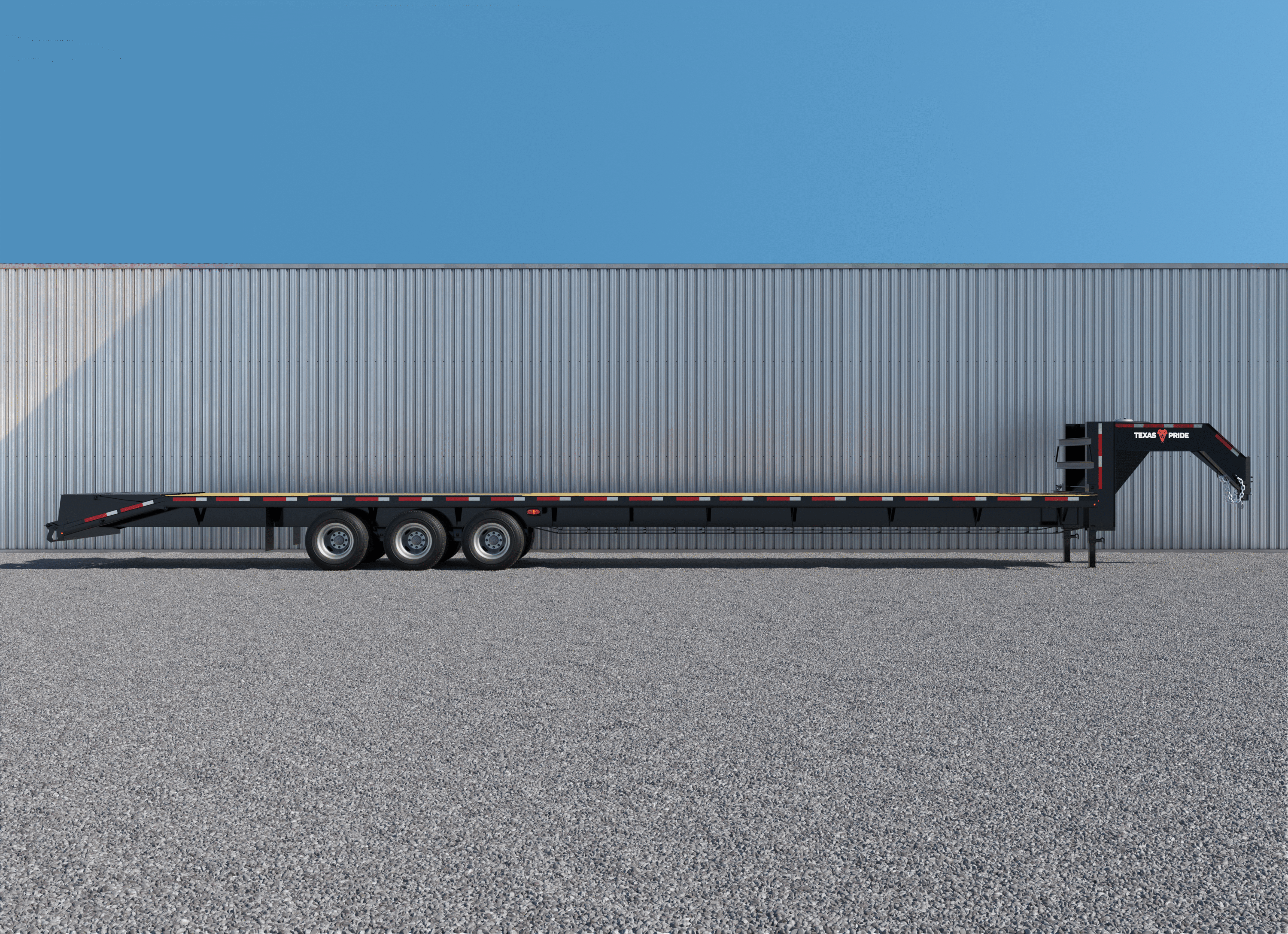 A Texas Pride Trailers Flatbed 36K 8×40+5 Gooseneck Triple Axle Dual Wheel is shown from the side, parked on a gravel lot against a corrugated metal building. The long, black steel trailer features reflective tape along the sides, three axles with dual wheels, and a gooseneck hitch, positioned under clear blue skies and bright sunlight.