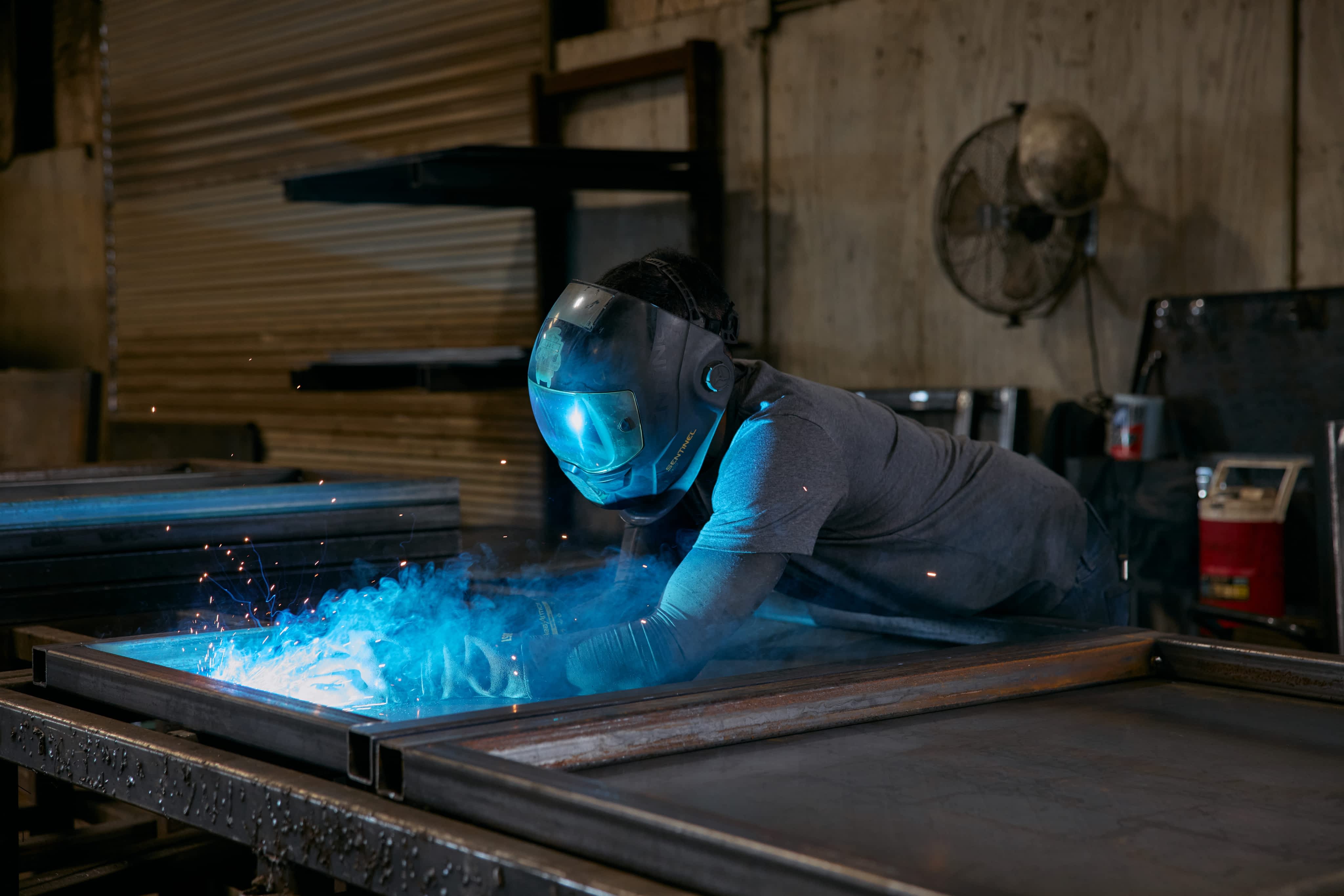 Welder in protective gear working on a metal trailer frame at a Texas Pride manufacturing facility.