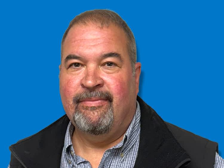 Texas Pride Trailers Location Manager in Stratford, Texas with a bald head and trimmed beard, smiling in a black collared shirt in front of a blue background.